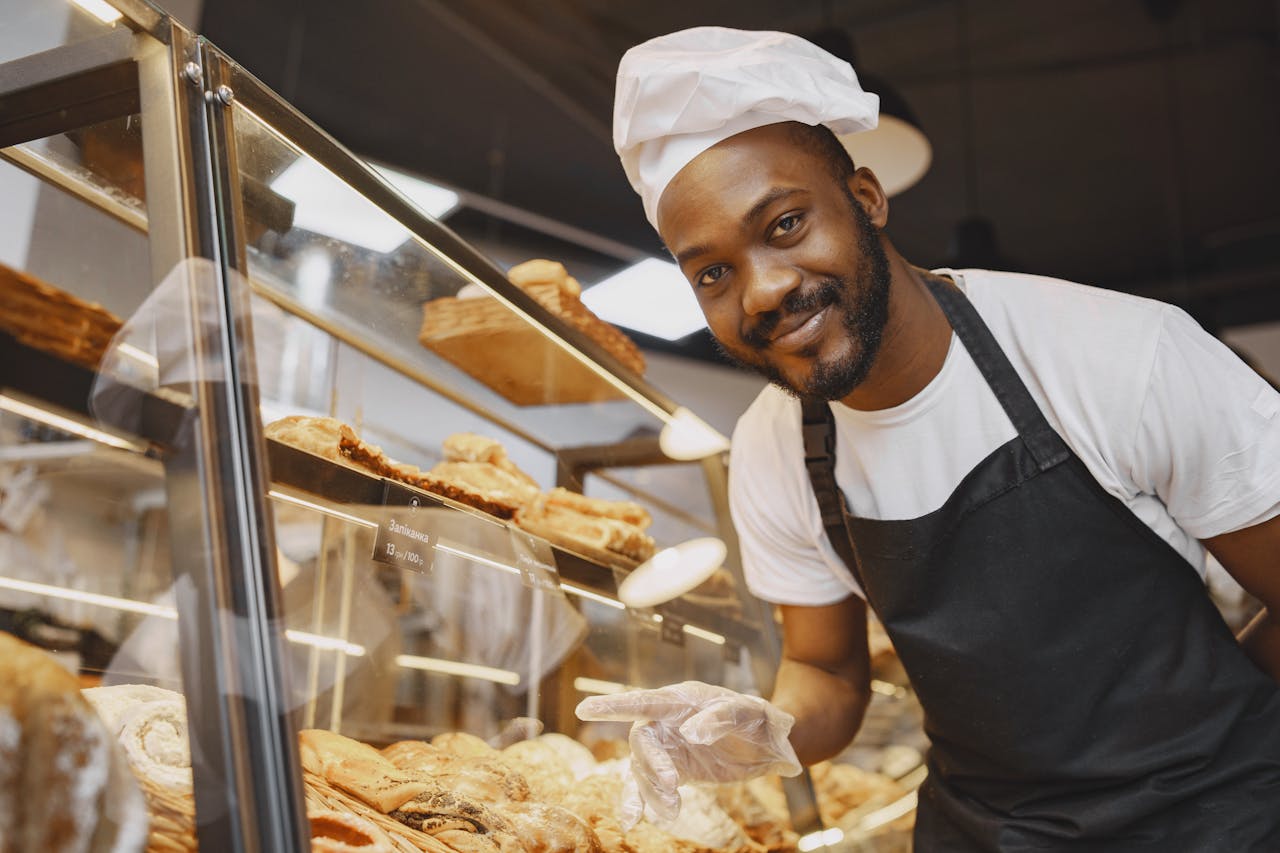 A baker looking at the camera, standing in front of a rack of bread.